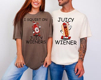 May include: Two t-shirts with humorous graphics. One is brown with a ketchup bottle character and the text "I SQUIRT ON JUICY WIENERS." The other is cream-colored with a hot dog character and the text "JUICY WIENER."