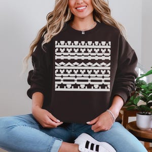 May include: A dark brown sweatshirt with a geometric white pattern across the front. The pattern consists of various shapes, including rectangles, triangles, and lines. The sweatshirt is a casual style, suitable for everyday wear.