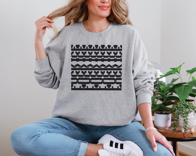 May include: A light gray sweatshirt with a black geometric pattern. The pattern is composed of various shapes, including rectangles, triangles, and lines. The sweatshirt is a crew neck style.