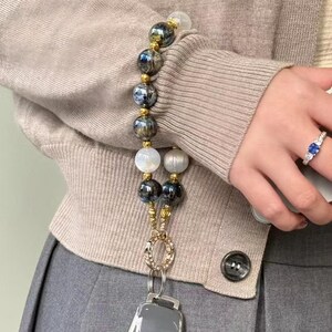 May include: A silver key chain with a black and white beaded strap. The strap has a gold ring and a silver key fob attached to it. The key fob has a silver button and a silver logo.
