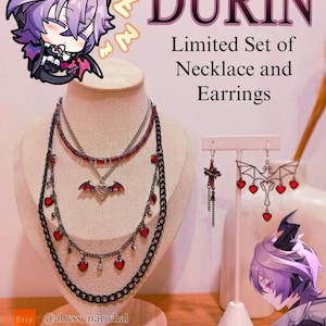 Puede incluir: Un conjunto limitado de collar y pendientes. Los collares presentan cadenas negras con detalles de corazones y gemas rojas, y un colgante de murciélago. Los pendientes tienen un diseño de alas de murciélago con detalles de corazones rojos. La palabra "DURIN" se muestra en rosa.