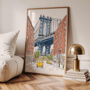 May include: A framed art print depicting a street scene with the Manhattan Bridge in New York City. The artwork features a blue bridge, red brick buildings, yellow taxis, and green trees. The print is displayed on a wall.