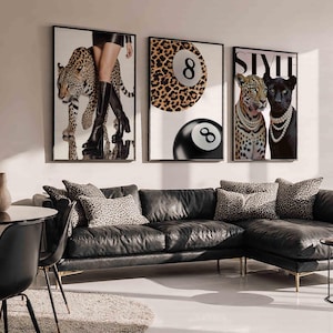 May include: Three framed art prints featuring a leopard, a pool ball with the number 8, and two big cats with pearl necklaces. The prints hang above a black leather sectional sofa with leopard print pillows.