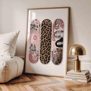 Op de afbeelding: Ingelijste kunst met drie skateboard decks. De decks tonen verschillende ontwerpen: een luipaardprint, een roze deck met een discobal en vrouwen, en een deck met een zebraprint en vrouwen. Het kunstwerk is ingelijst in een licht houten frame.