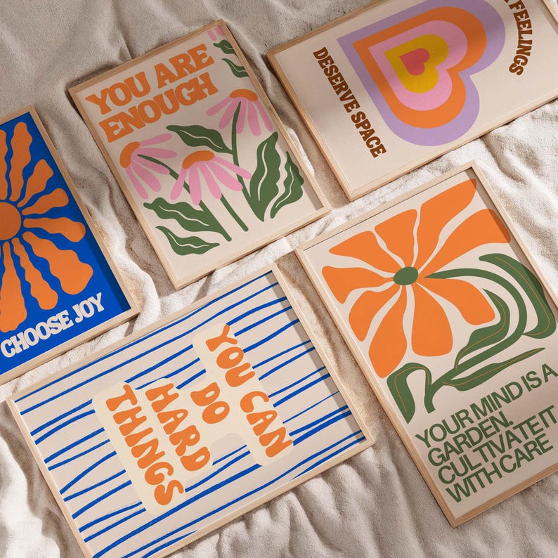 May include: A collection of framed art prints with inspirational quotes and floral designs. The prints feature phrases like "You are Enough" and "Choose Joy" in orange and blue hues. The artwork includes a heart and flower illustrations.