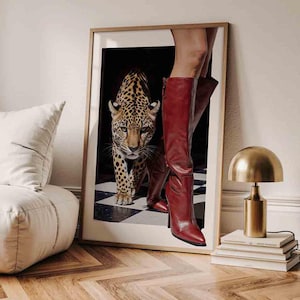 Puede incluir: Impresión artística enmarcada que presenta un leopardo y botas rojas hasta la rodilla. El leopardo está en el centro, sobre un suelo a cuadros blanco y negro. Las botas están a la derecha. La obra está en un marco de madera.