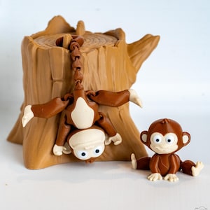 May include: A brown and tan monkey-themed toy set. The set includes a tree stump, a monkey hanging upside down, and a sitting monkey. The monkeys have white faces and hands and feet. The tree stump is brown with a textured surface.