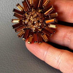 May include: A gold-toned brooch with a round, sparkly centre surrounded by a ring of amber-coloured, rectangular stones.