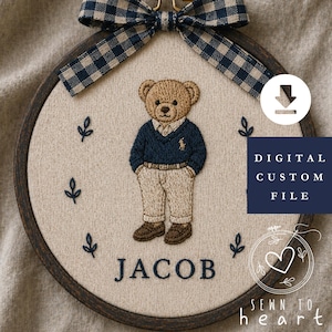 May include: Embroidered teddy bear wearing a blue sweater and khaki trousers, with the name "JACOB" stitched below. The design is set in a wooden embroidery hoop, adorned with a plaid bow at the top. The words "DIGITAL CUSTOM FILE" are visible.