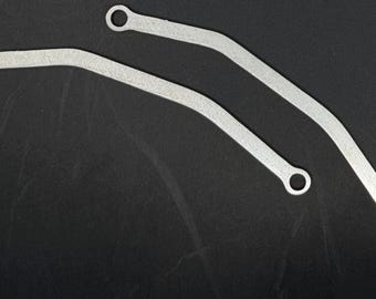 Op de afbeelding: Twee zilverkleurige metalen steunarmen met een gebogen, langwerpige vorm. Elke arm is voorzien van een cirkelvormig oogje aan beide uiteinden, wat een veilig bevestigingspunt biedt. Het metalen oppervlak heeft een licht getextureerde, matte afwerking.