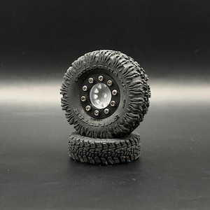 May include: Two black off-road vehicle tires stacked on top of each other. The tires have a deep tread pattern and a silver hub with multiple lug nuts. The sidewall of the tire has the text "PATAGONIA MT" and "THE HESTAR".