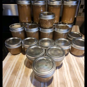 May include: A collection of 15 glass jars with silver lids filled with a brown liquid. The jars are arranged in a pyramid shape on a striped surface.