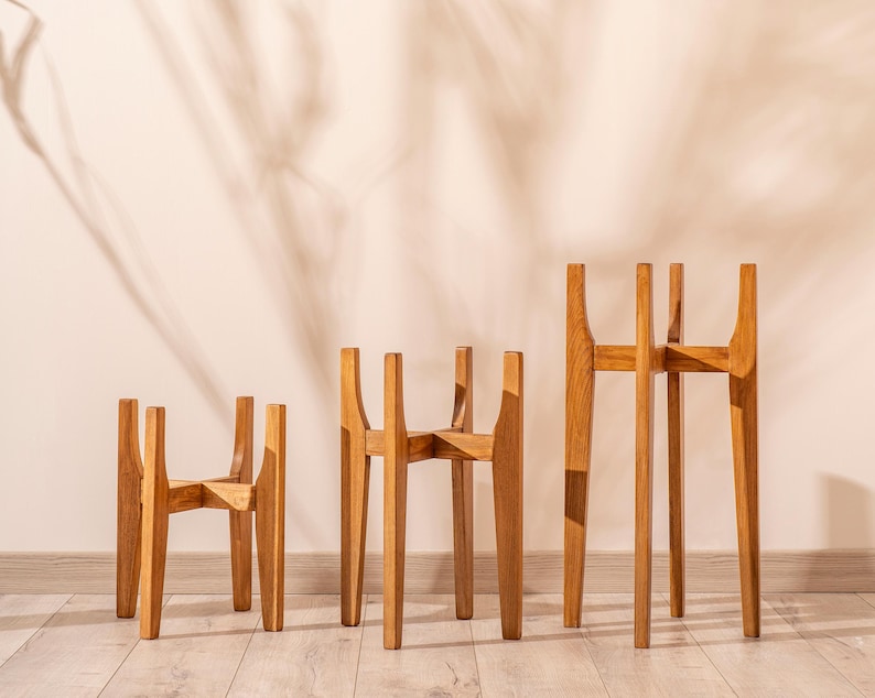 May include: Three wooden plant stands of varying heights. The stands are made of natural wood and have a simple, modern design. They are perfect for displaying plants or other decorative items.