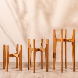 May include: Three wooden plant stands of varying heights. The stands are made of natural wood and have a simple, modern design. They are perfect for displaying plants or other decorative items.