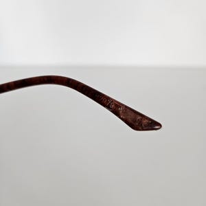 Puede incluir: Primer plano de una patilla de gafas marr&oacute;n. La patilla es curva y se estrecha hasta un punto. El texto "H2979" es visible en la patilla. La montura parece estar hecha de un material oscuro, posiblemente vintage.