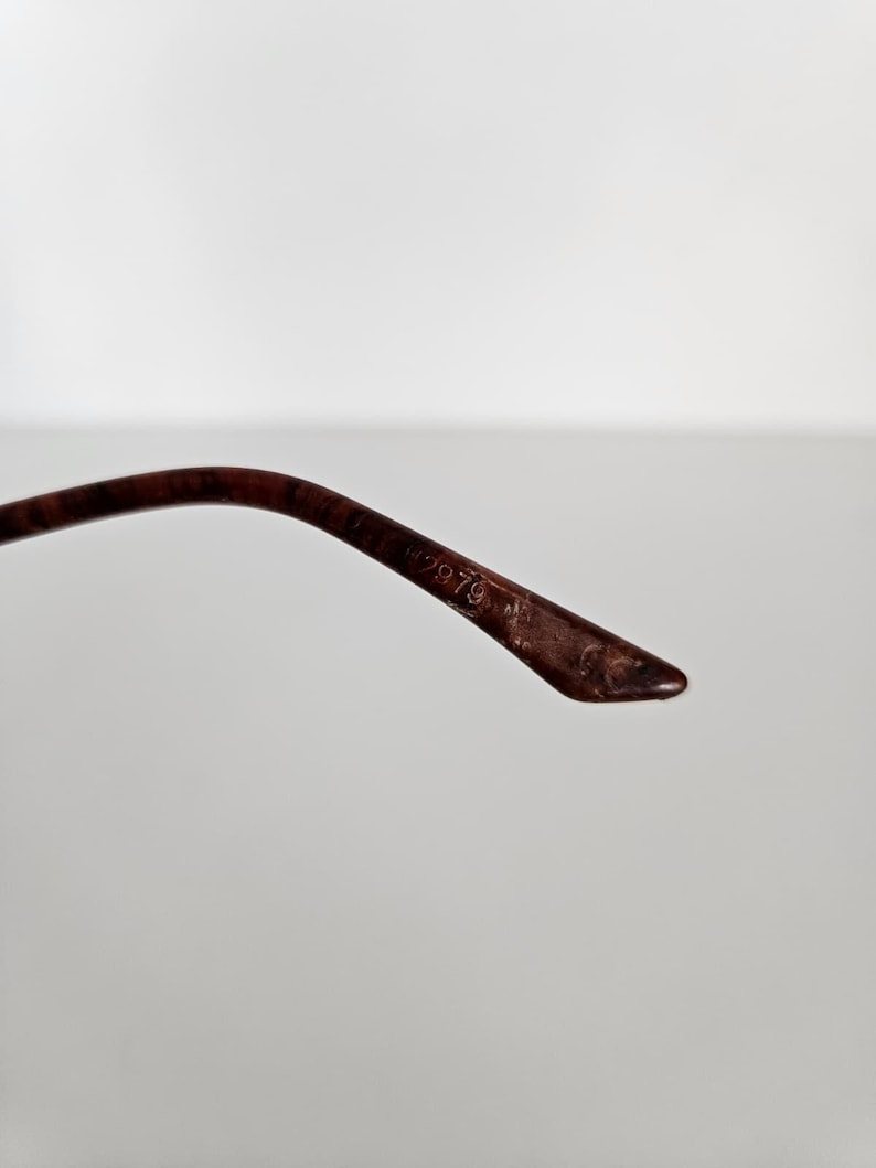 Puede incluir: Primer plano de una patilla de gafas marr&oacute;n. La patilla es curva y se estrecha hasta un punto. El texto "H2979" es visible en la patilla. La montura parece estar hecha de un material oscuro, posiblemente vintage.