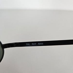 Puede incluir: Gafas de sol negras con el texto "B&L RAY-BAN" impreso en blanco en la varilla. Las gafas de sol tienen un dise&ntilde;o cl&aacute;sico, con montura y lentes oscuras.