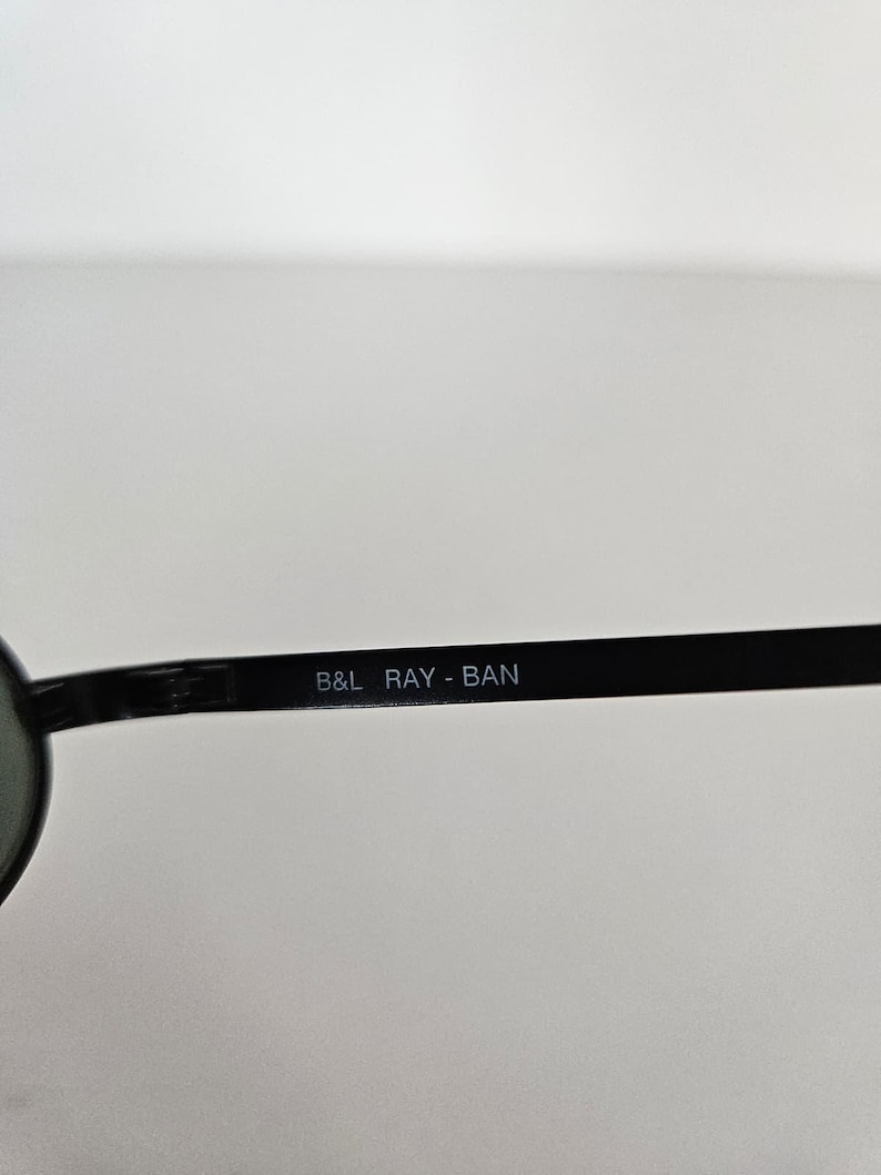 Puede incluir: Gafas de sol negras con el texto "B&L RAY-BAN" impreso en blanco en la varilla. Las gafas de sol tienen un dise&ntilde;o cl&aacute;sico, con montura y lentes oscuras.
