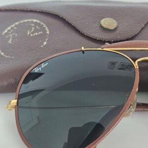Puede incluir: Gafas de sol de cuero marr&oacute;n con lentes oscuras y montura dorada. Las gafas de sol est&aacute;n en un estuche de cuero marr&oacute;n con el logotipo de Ray-Ban. El estuche tiene un cierre de bot&oacute;n.