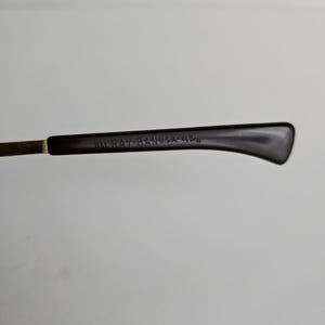 Pu&ograve; includere: Un'asta di occhiali marrone scuro con una cerniera in metallo color oro. Il lato interno del terminale presenta il testo in rilievo B&L RAY-BAN U.S.A. 43/14, che indica il marchio e le misure specifiche della montatura degli occhiali.