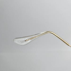 May include: Close-up of a clear, plastic eyeglass temple tip with the text "HORSE" printed on it. The temple arm is gold-colored and curves away from the tip. The background is a plain, light gray.