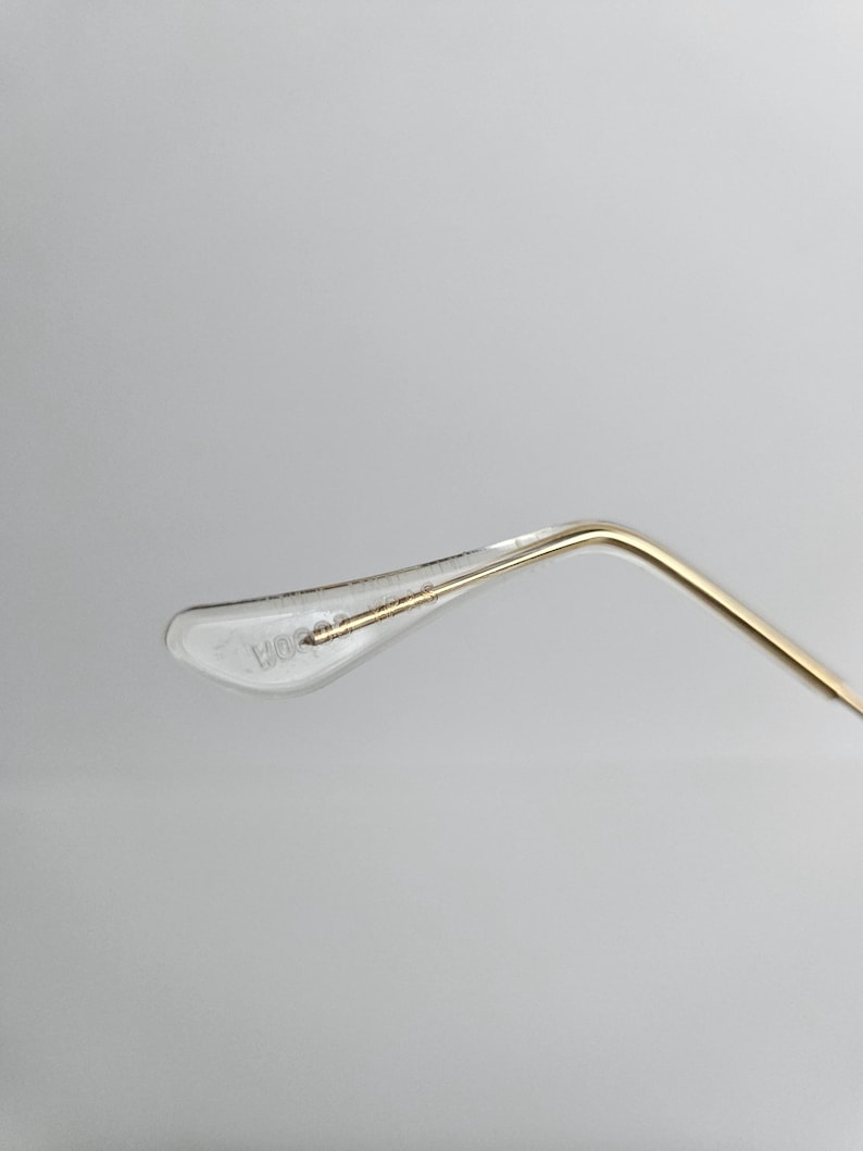 May include: Close-up of a clear, plastic eyeglass temple tip with the text "HORSE" printed on it. The temple arm is gold-colored and curves away from the tip. The background is a plain, light gray.