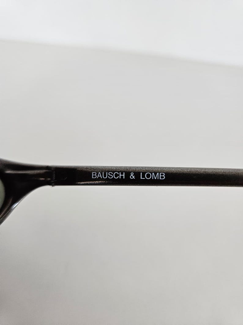 May include: Close-up of a dark-colored eyeglass frame with the text "BAUSCH & LOMB" printed in white. The frame is set against a plain white background.