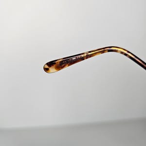 May include: Close-up of a tortoiseshell-patterned eyeglass arm. The arm curves gently and has a rounded tip. The text "21016 NO. 3" is printed on the arm. The color palette includes shades of brown, tan, and black.
