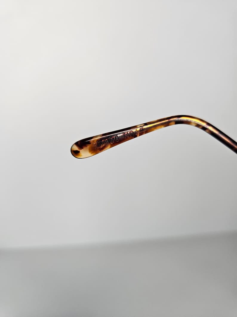 May include: Close-up of a tortoiseshell-patterned eyeglass arm. The arm curves gently and has a rounded tip. The text "21016 NO. 3" is printed on the arm. The color palette includes shades of brown, tan, and black.