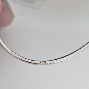 以下が含まれることがあります： 銀色の縁取りと反射面を持つ丸いオブジェクトのクローズアップ。縁には小さな黒い点があり、摩耗の兆候が見られます。オブジェクトは人の手で持たれており、左上隅に部分的に見えています。