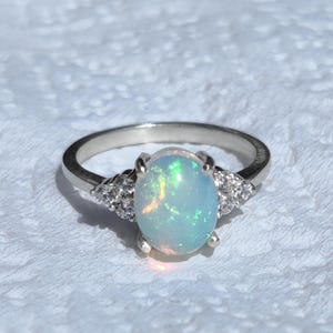May include: A silver ring with a large oval opal gemstone and smaller clear gemstones on the band.