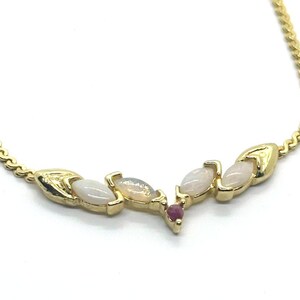 May include: A gold-tone necklace featuring a V-shaped centerpiece adorned with four marquise-cut opals and a single small round red gemstone at the bottom point. The chain is a delicate link style that connects to the decorative metal settings.