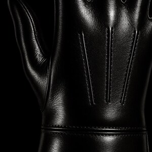 May include: Black leather gloves with a smooth, shiny finish. The gloves have a seam down the center of each finger and a seam around the wrist.