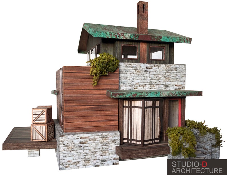 K&ouml;nnte beinhalten: Ein Modell eines kleinen, rustikalen Hauses mit einem gr&uuml;nen Dach, Steinmauern und Holzverkleidung. Das Haus hat eine kleine Veranda mit einem Holzgel&auml;nder und ein paar Holzkisten auf der Veranda. Das Haus ist aus Papier und Teil eines Papiermodellbausatzes.