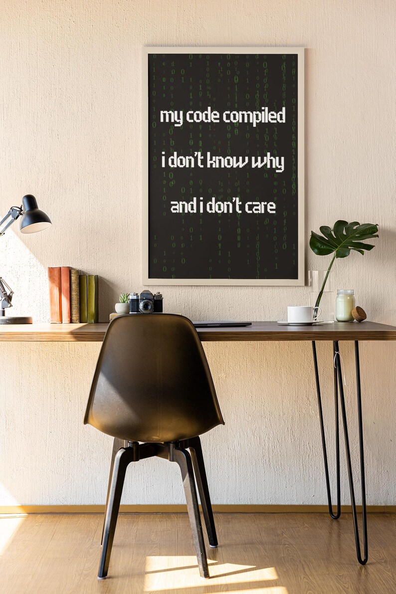 Pu&ograve; includere: Una stampa incorniciata con sfondo nero e testo bianco che recita "my code compiled i don't know why and i don't care". Il testo &egrave; circondato da una matrice verde di numeri.