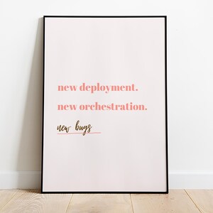 Peut inclure: Une impression encadrée avec un fond rose et un cadre noir. Le texte sur l'impression est "new deployment. new orchestration. new bugs".