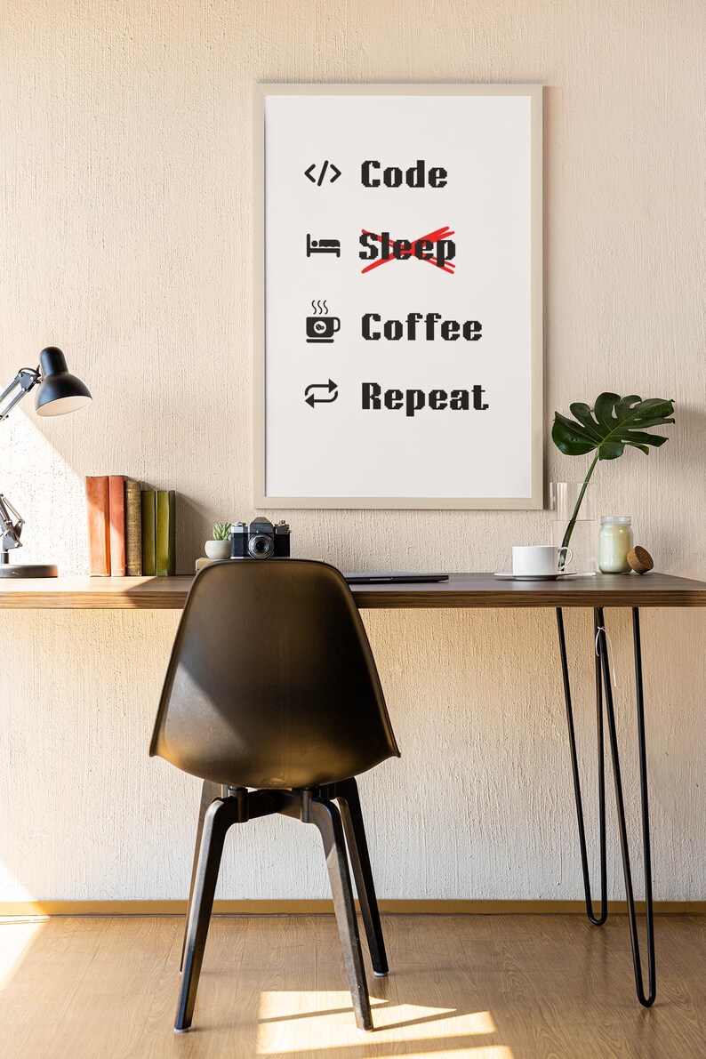 Pode incluir: Uma impress&atilde;o emoldurada com fundo branco e texto preto que diz "</> Code,  Sleep, Coffee, Repeat." A impress&atilde;o est&aacute; pendurada em uma parede bege acima de uma mesa de madeira com uma cadeira preta.