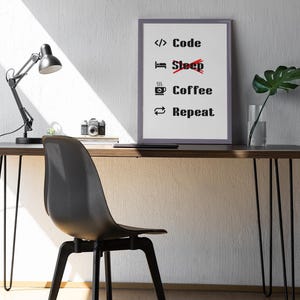 Pode incluir: Uma impress&atilde;o emoldurada com o texto "Code Coffee Repeat" com uma linha vermelha atravessando a palavra "Sleep". A impress&atilde;o est&aacute; pendurada em uma parede branca acima de uma mesa com uma cadeira preta, uma l&acirc;mpada e uma planta em vaso.