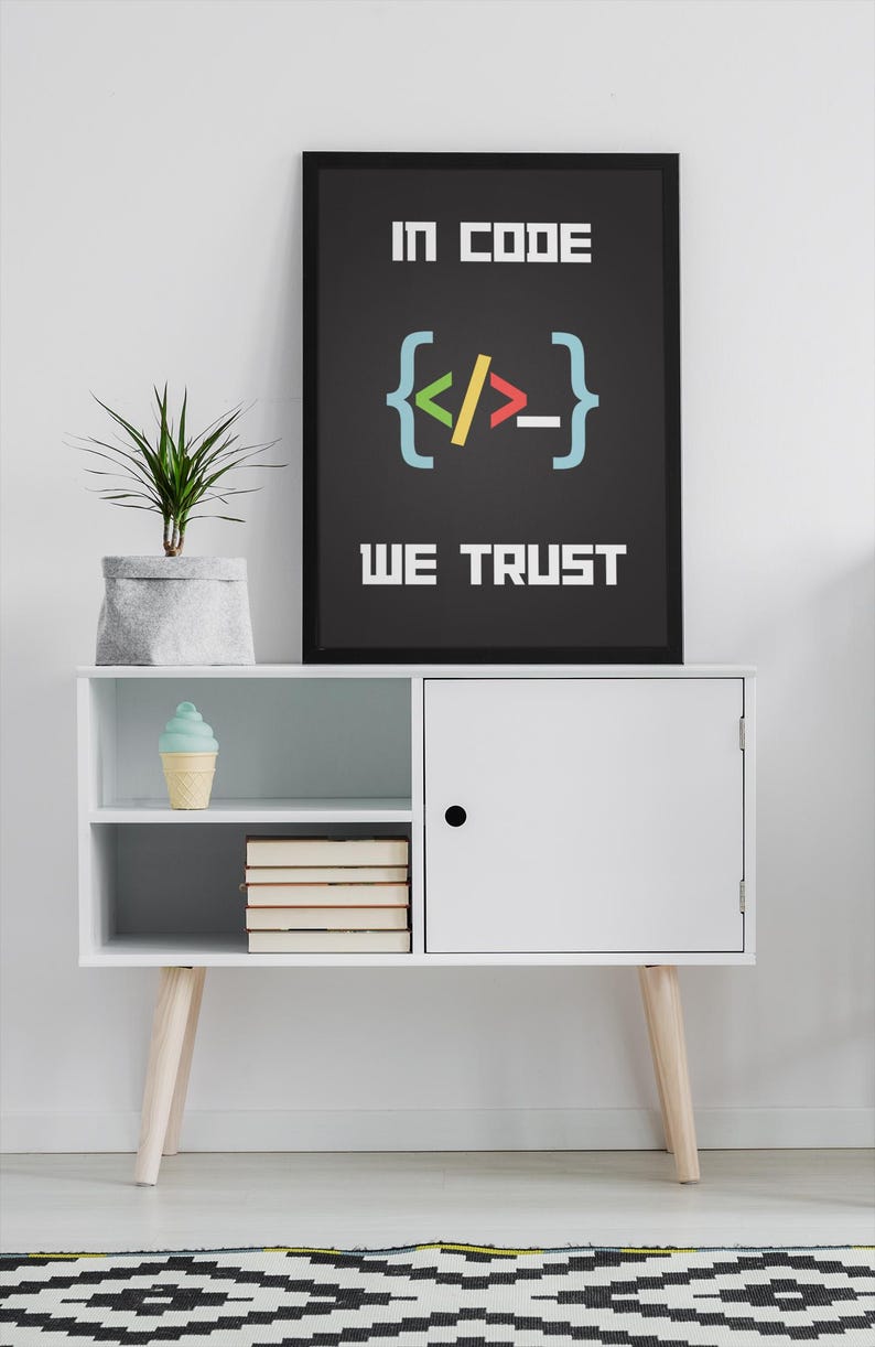 Puede incluir: Un armario blanco con una puerta negra y dos estantes. El estante superior tiene un cono de helado azul y blanco. El estante inferior tiene una pila de libros. Un p&oacute;ster enmarcado negro con el texto "In code we trust" y un s&iacute;mbolo de corchete de c&oacute;digo colorido est&aacute; colgado en la pared sobre el armario.