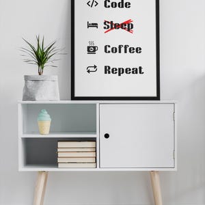 Pode incluir: Um arm&aacute;rio branco com uma porta preta e duas prateleiras. A prateleira superior tem um cone de sorvete azul e branco. A prateleira inferior tem uma pilha de livros. Um p&ocirc;ster preto emoldurado com texto branco diz "Code Coffee Repeat" com uma linha vermelha atrav&eacute;s da palavra "Sleep". Uma planta verde em um vaso cinza est&aacute; em cima do arm&aacute;rio.