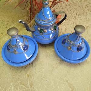 Może przedstawiać: Zestaw trzech niebieskich ceramicznych czajników z srebrnymi akcentami i niebieskimi i zielonymi kamieniami szlachetnymi. Czajniki są ozdobione misternymi wzorami.
