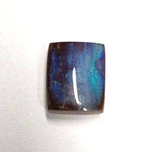 May include: A rectangular gemstone with rounded corners. The stone has a dark brown border and a centre with swirling blue and teal colours. The stone is set against a white background.