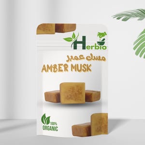 May include: A transparent pouch displaying 'Amber Musk' in English and Arabic script. Inside are several amber-hued, square blocks. The Herbio logo and '100% Organic' are also visible. The product is likely a natural fragrance.
