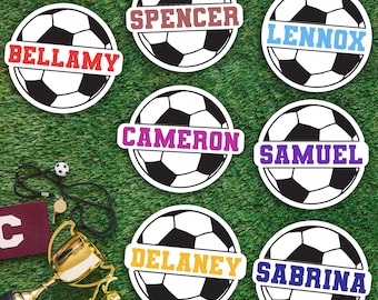 Può includere: Cerchi a forma di pallone da calcio con nomi come Bellamy, Spencer, Lennox, Cameron, Samuel, Delaney e Sabrina. I nomi sono in diversi colori. Su uno sfondo verde, con accessori calcistici come trofei e un fischietto.