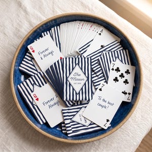 May include: A deck of playing cards with a navy blue and white vertical stripe pattern, housed in a blue ceramic bowl. The cards feature custom text including "Forever & Always," "The Mason EST. 2020," and "To the best couple!" alongside standard card suits.