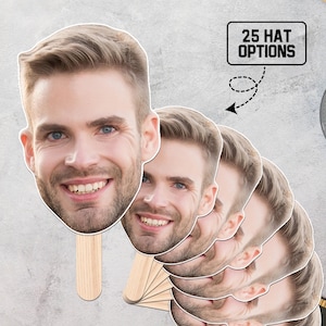 May include: A stack of face fans featuring a smiling man with light brown hair and blue eyes. Each fan has a wooden handle. The text "25 HAT OPTIONS" is in a black box with a dotted arrow pointing to the fans.