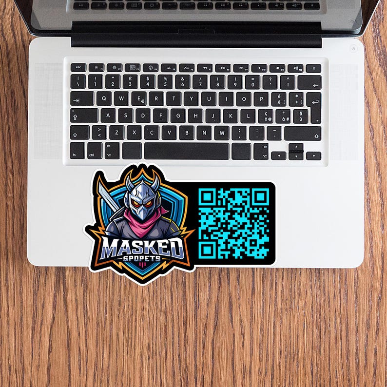 May include: A sticker featuring a masked character with a sword, set against a blue shield. The text "MASKED SPOPETS" is below the character. A QR code is on the right side of the sticker. The sticker is on a laptop.