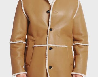 May include: A tan leather coat with a white shearling collar and trim. The coat has a button-up front and two pockets. The sleeves have white shearling trim at the cuffs. The coat is a mid-length style.