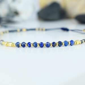 May include: A delicate bracelet featuring faceted blue lapis lazuli beads interspersed with gold-colored metal accents. The adjustable cord is a dark blue-gray color, creating a minimalist and elegant design. The bracelet is suitable for everyday wear.