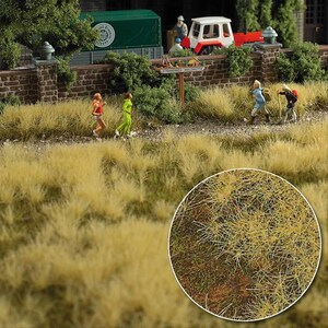 May include: A miniature diorama featuring a field of tall, dry, yellow-toned grass with a circular inset showing a detailed close-up of the texture. The scene includes small scale figures of people walking and running, a brick wall, and a tractor.